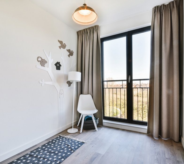 Minimalist style chair and lamp placed near window with curtains and cartoon tree decoration in corner of kid room